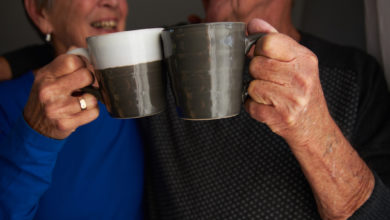 Senior couple who are residents of a long-term care community toasting mugs of coffee or tea