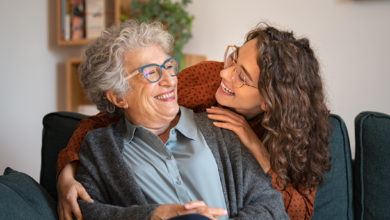 Young adult caretaker with glasses laughing with senior in assisted living