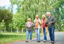 Group of four senior friends walking outdoors in greenway at independent living community