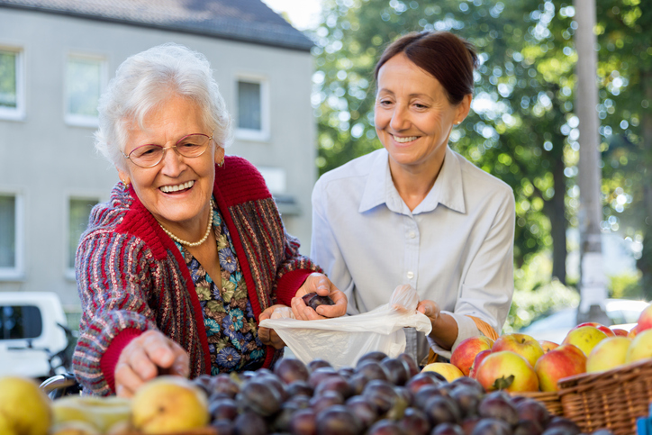 senior woman shopping at a fruit stand with a caregiver