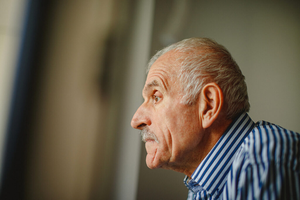 A senior man with a mustache looks ahead, unsure and worried.