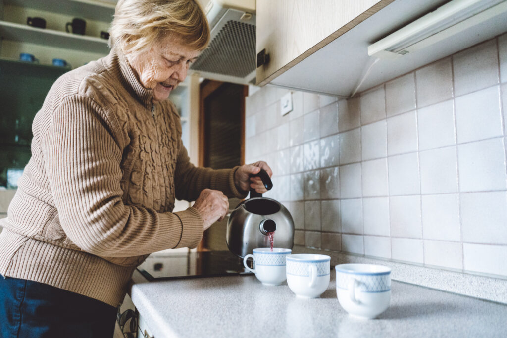 senior woman pouring tea from a kettle into multiple teacups