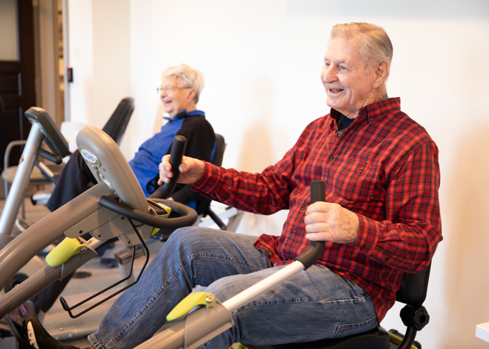 Smiling senior man and woman use exercise equipment in a senior living community