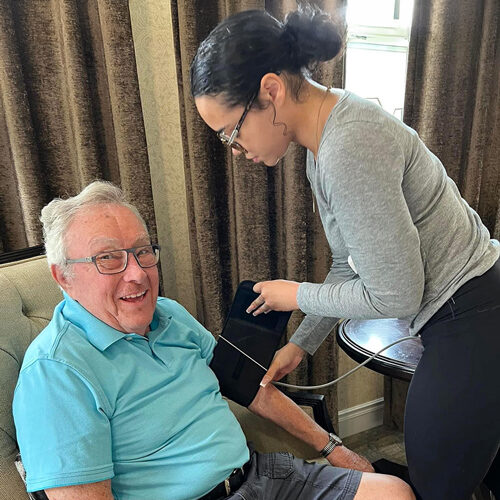 smiling senior man seated in a chair getting his blood pressure taken by a young woman